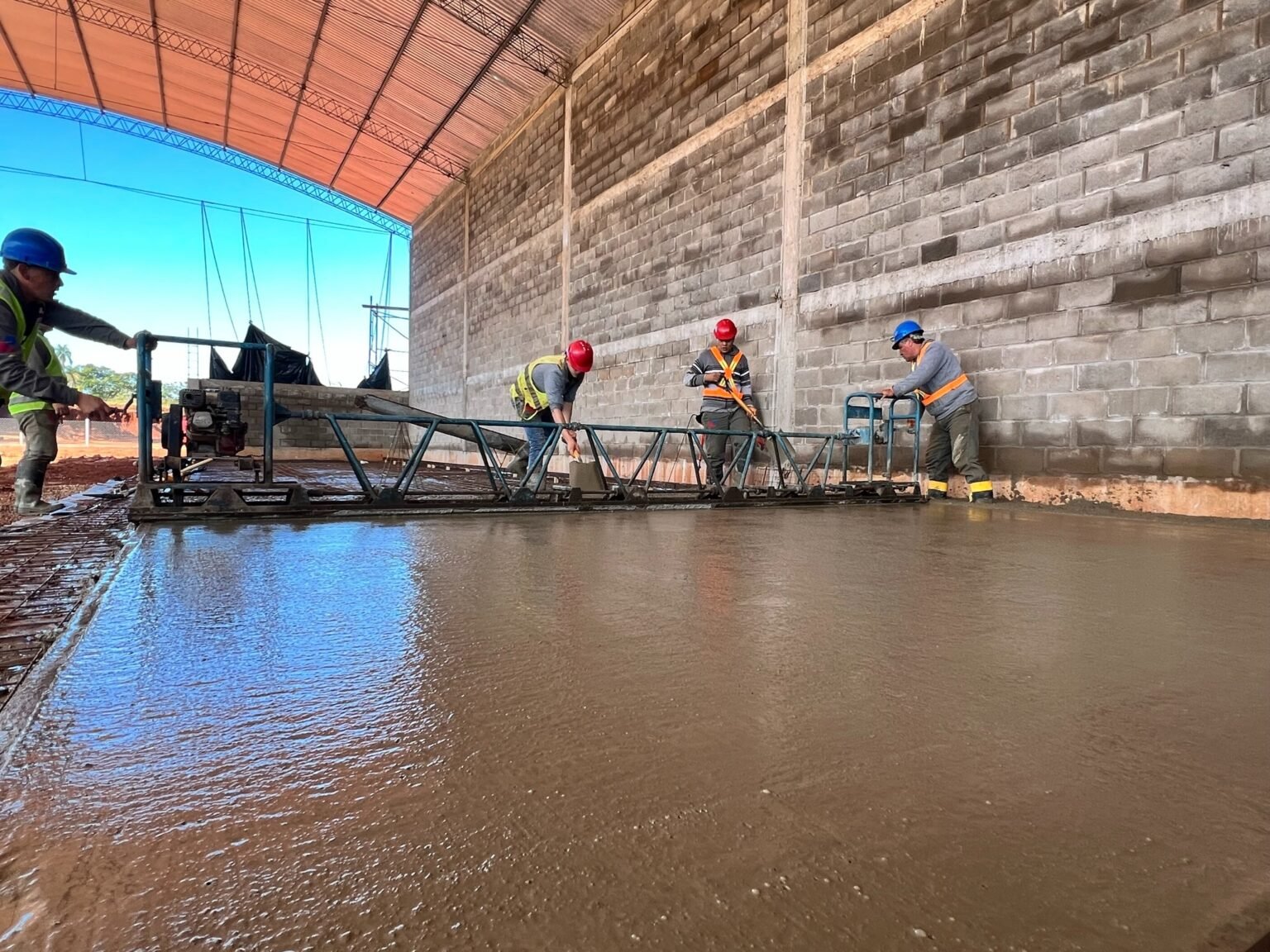 Equipo con cascos y chalecos trabajando con una regla de nivelación sobre un piso de hormigón