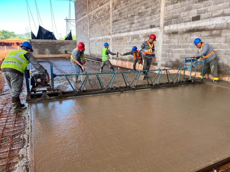 Equipo con cascos y chalecos nivelando hormigón con una regla