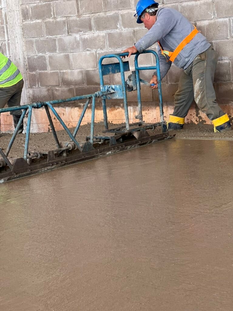 Operario con casco y chaleco trabajando en el extremo de la regla sobre el hormigón
